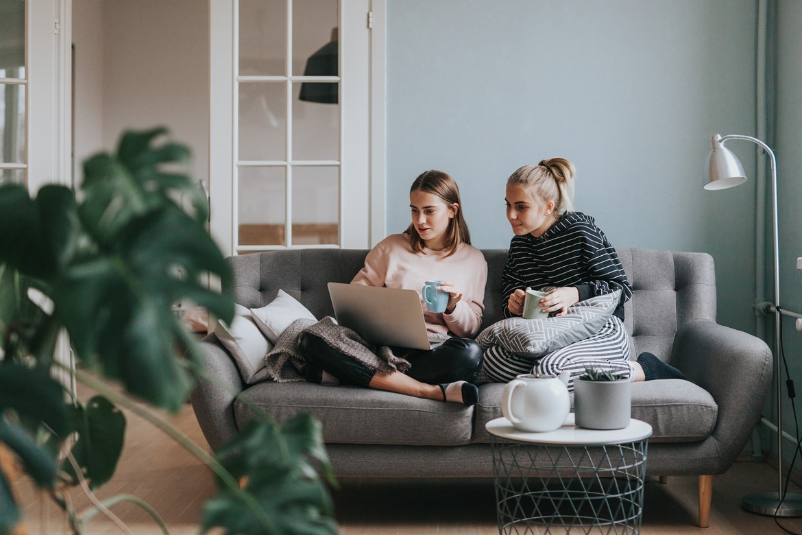 Two women sitting on a sofa together buying something on a laptop