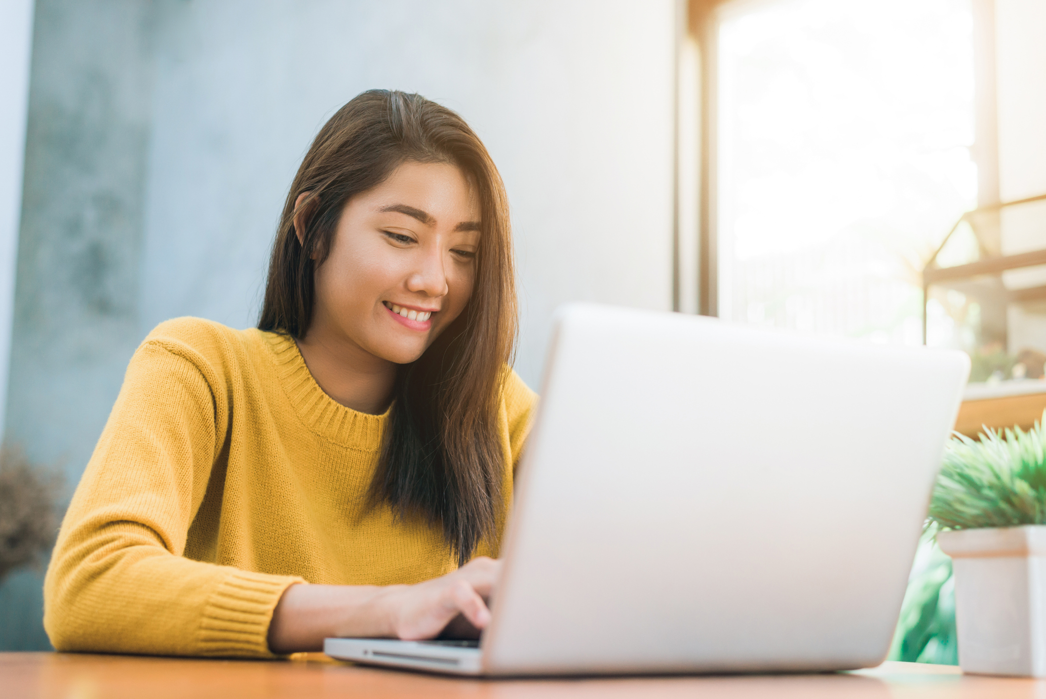 A woman in a yellow top reading her emails on a laptop