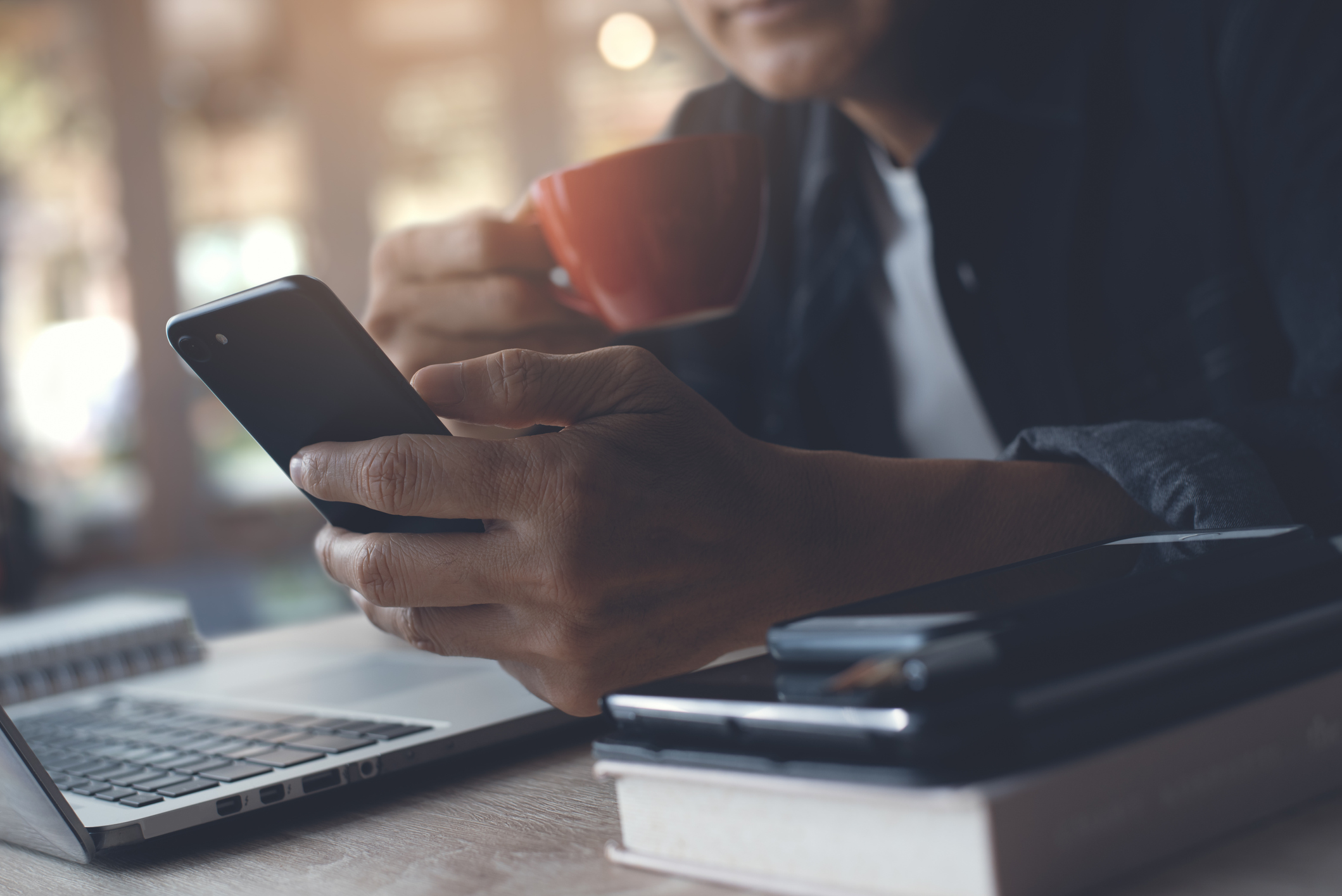 Man with a coffee looking at his phone with his laptop open