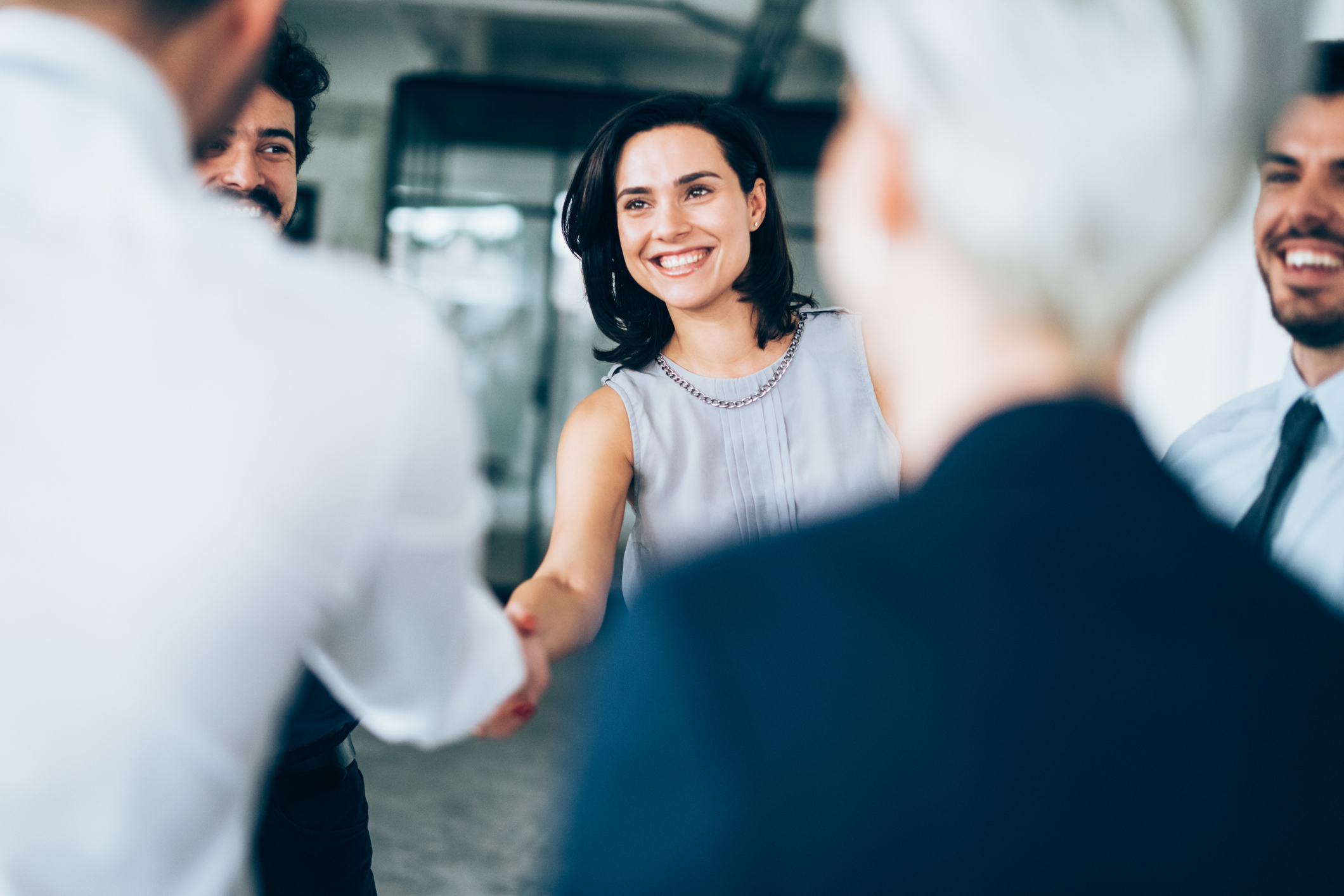 Businesswoman shaking hands with a man in a white shirt, with colleagues standing around them