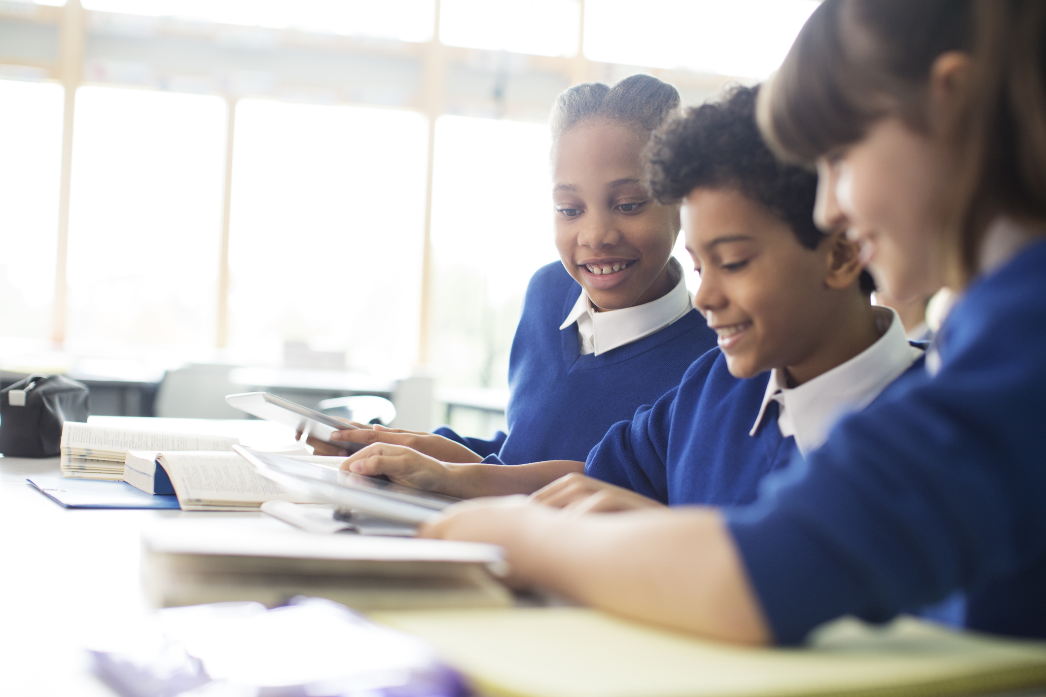 Three schoolchildren in blue jumpers studying in a classroom