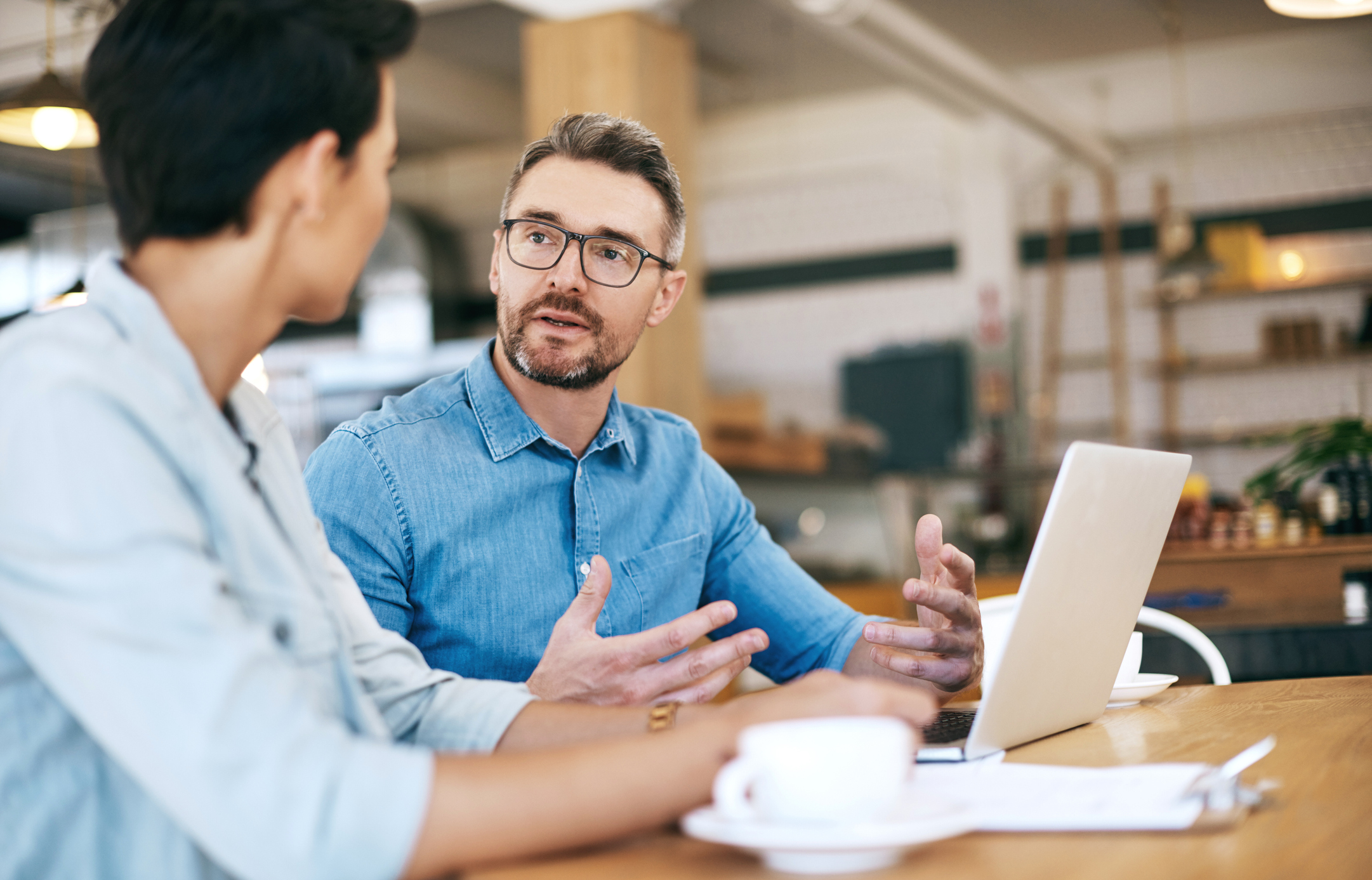 Two businesspeople talking over a coffee, looking at a laptop