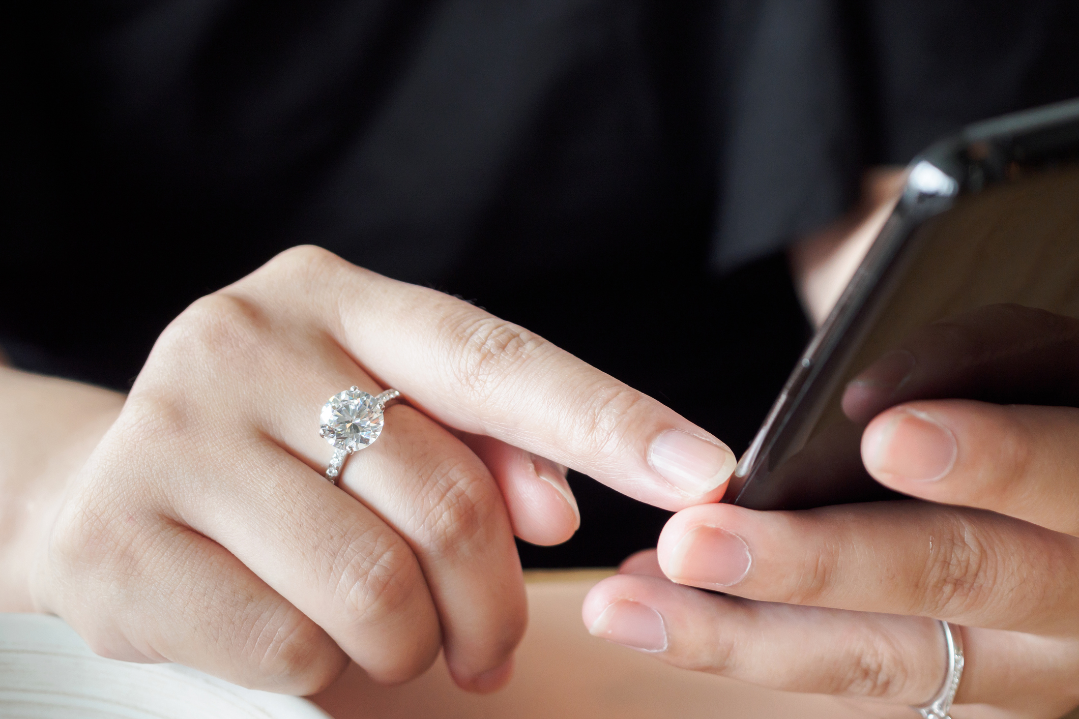 Woman wearing a large diamond engagement ring shopping on her phone for more jewellery