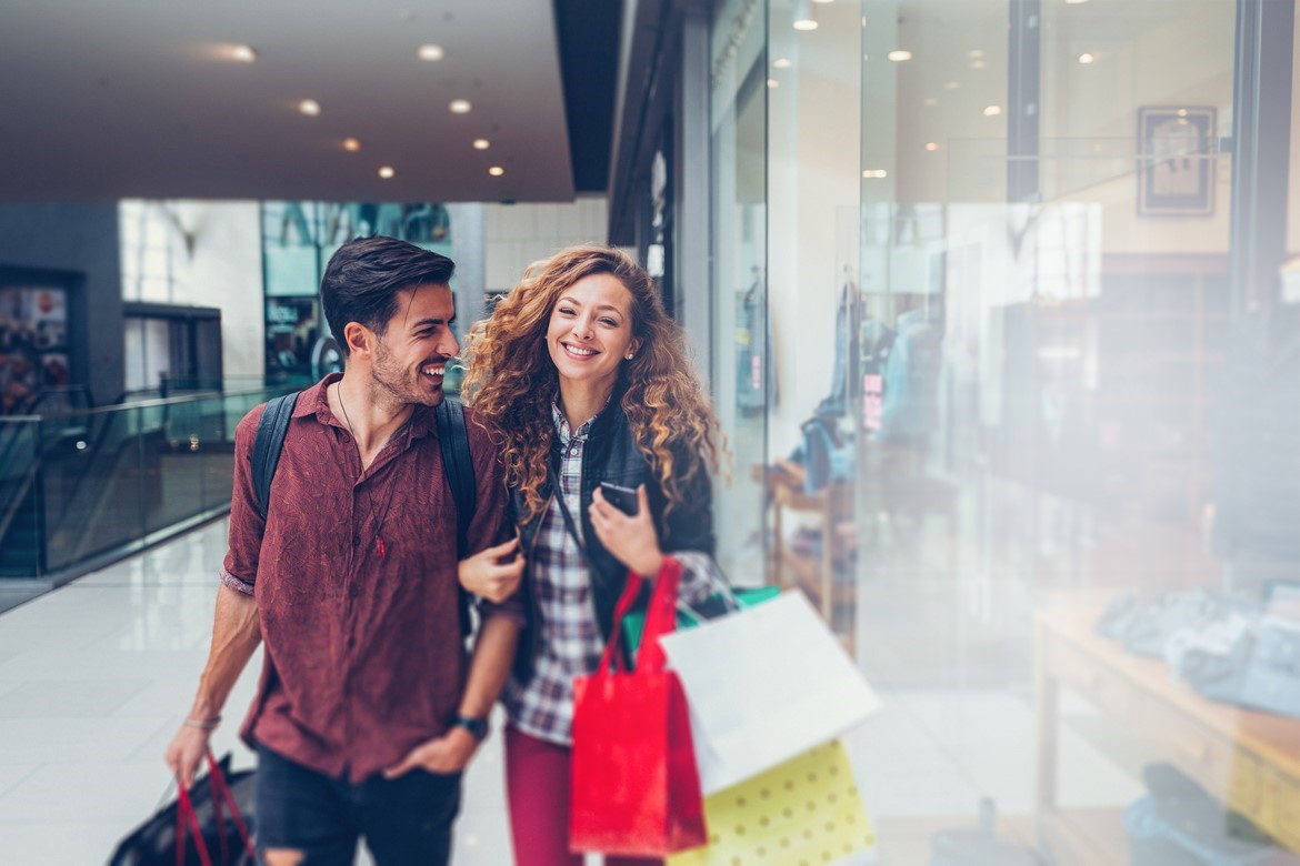 Young couple walking through a busy shopping centre carrying several shopping bags